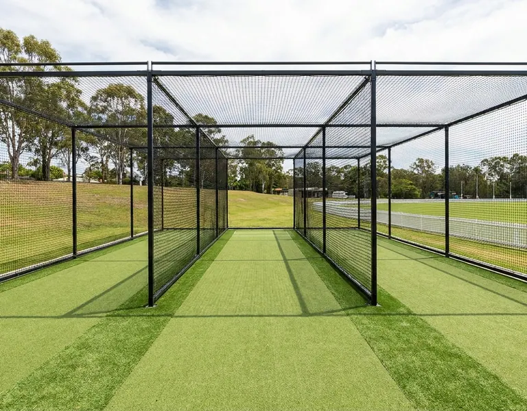 Cricket training nets with black steel frames over green synthetic pitches beside an oval