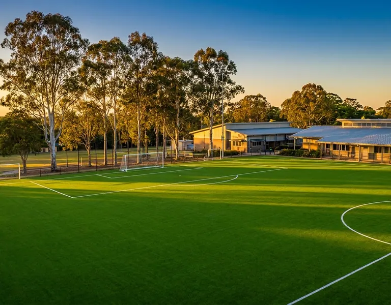 Synthetic turf sports field with white line markings beside school buildings at sunset