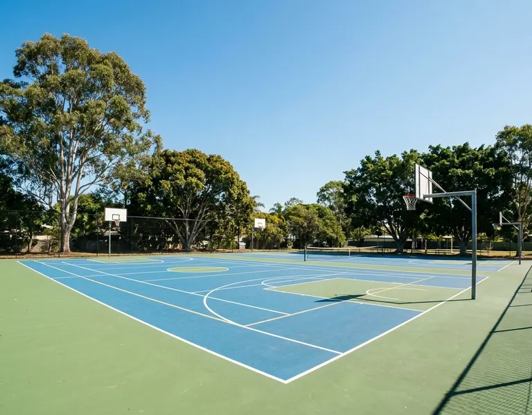 Fenced outdoor multi-sport court in blue and green with basketball hoops and line markings