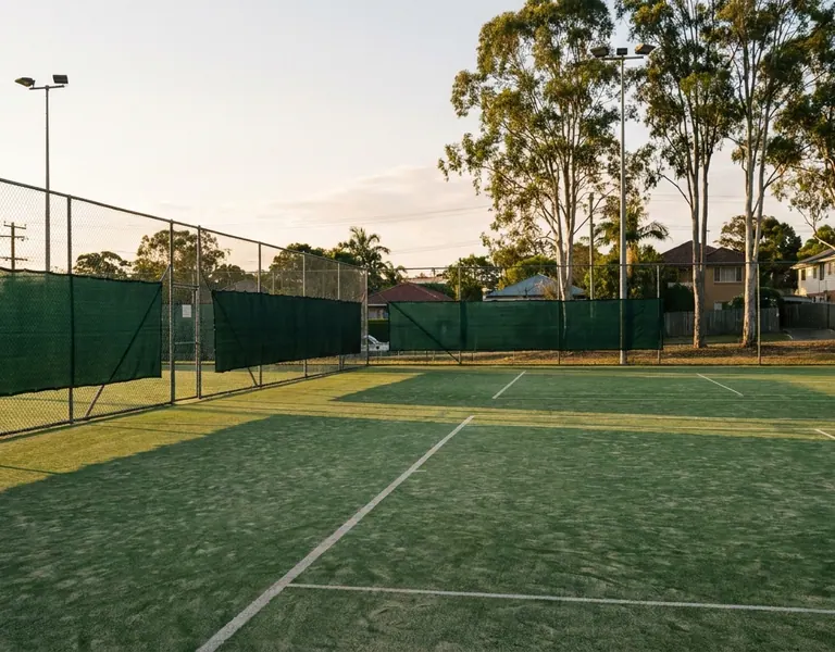 Synthetic grass tennis court with white lines, green windbreak fencing and tall gum trees